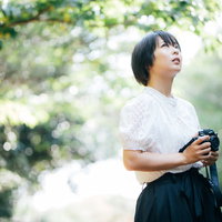 木漏れ日の中でミラーレスカメラを構えるカメラ女子の写真