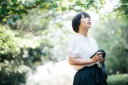 木漏れ日の中でミラーレスカメラを構えるカメラ女子