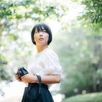 新緑の木漏れ日の中、撮影場所を探すカメラ女子の写真