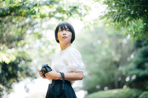 新緑の木漏れ日の中、撮影場所を探すカメラ女子