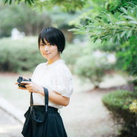 白いトップスを着た笑顔で会釈するカメラ女子の写真