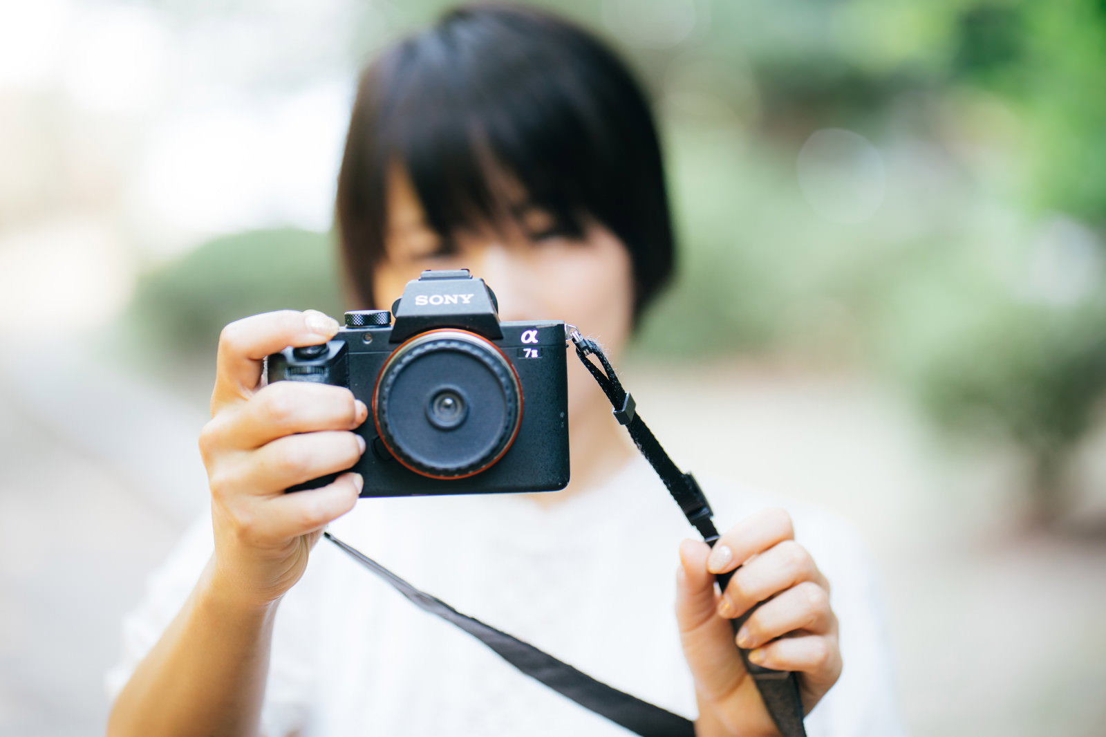 屋外でミラーレスカメラを両手で構えて撮影している女性［モデル：にゃるる］