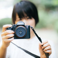 ミラーレスカメラを持って屋外で撮影する女性の写真