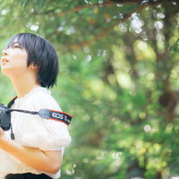 新緑の木漏れ日の中でカメラを構える女子フォトグラファーの写真