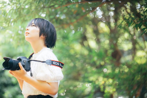 新緑の木漏れ日の中でカメラを構える女子フォトグラファー