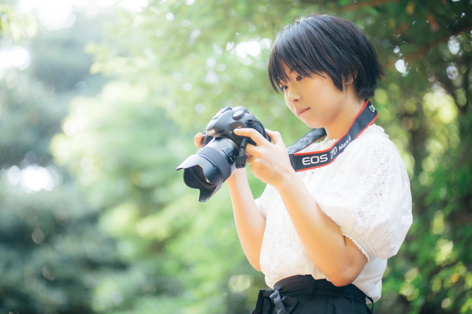 木漏れ日の中で一眼レフカメラの設定を確認するカメラ女子［モデル：にゃるる］