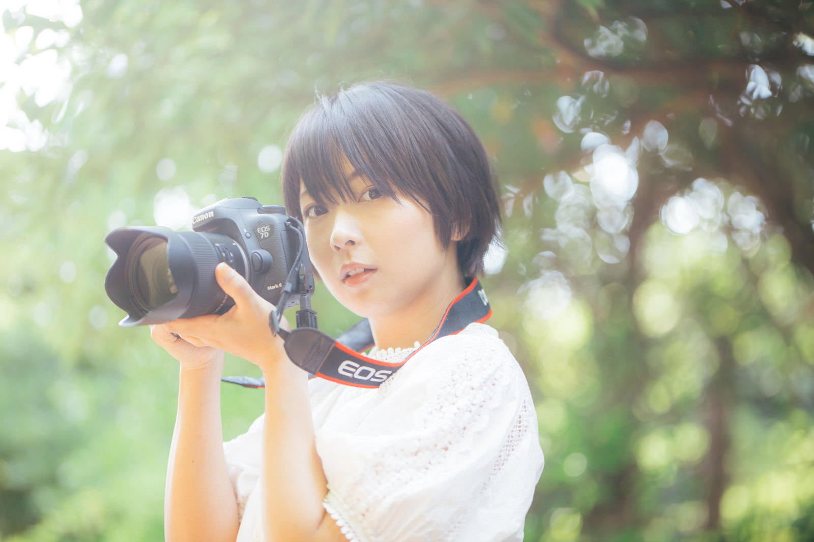 木漏れ日の中で一眼レフカメラを構える女性カメラ女子［モデル：にゃるる］