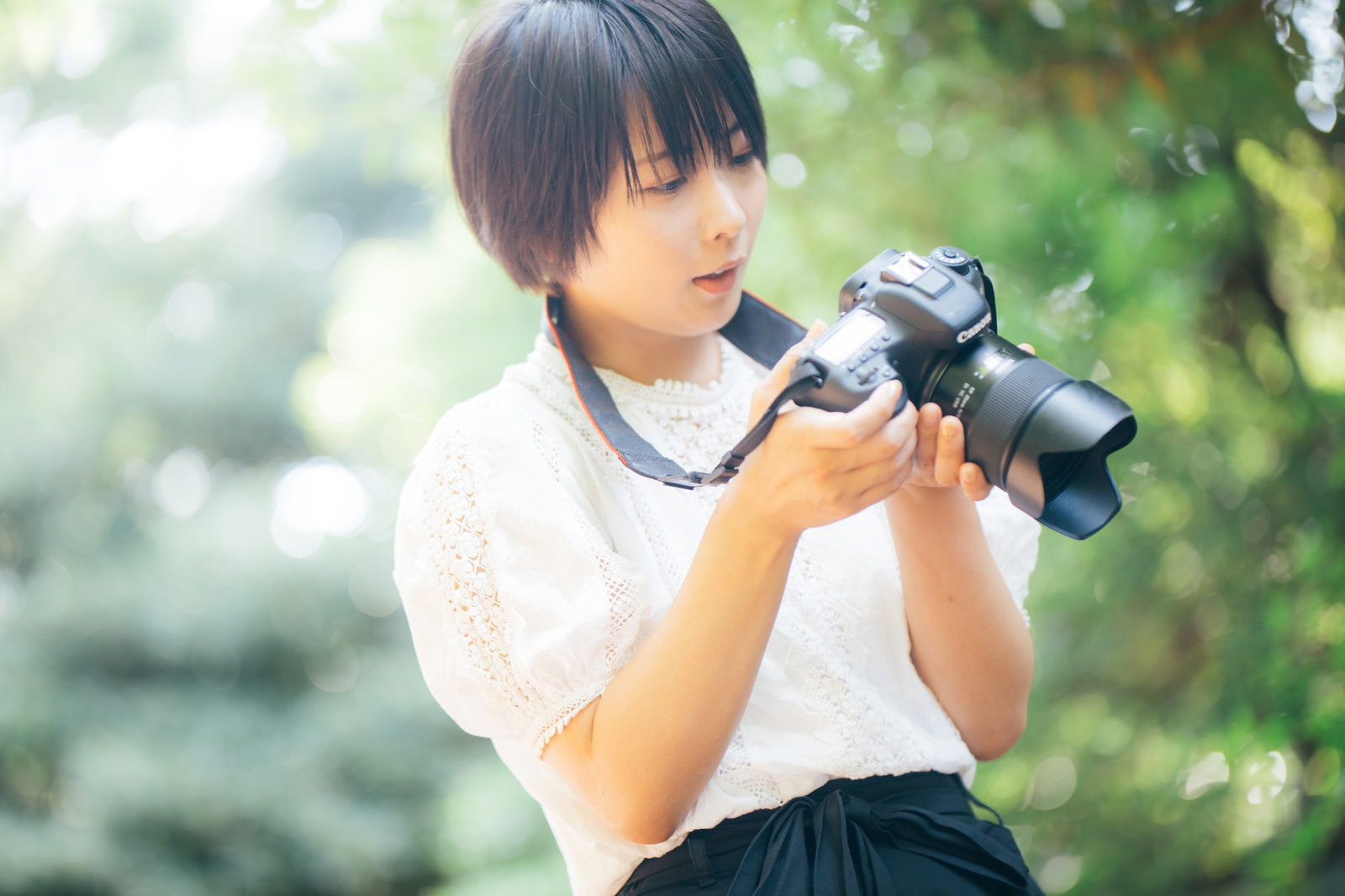 白いトップスを着た女性が一眼レフカメラを構えている様子［モデル：にゃるる］
