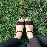 芝生の上で過ごす女性の足元とサンダル、黒いパンツの写真
