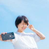 夏日の青空でピースサインをする自撮り女子の写真
