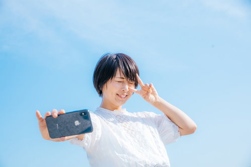 夏日の青空でピースサインをする自撮り女子