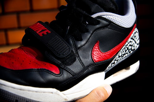 黒と赤のNIKEスニーカーをレンガ背景に手に持つ