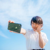 青空の下でスマートフォンで自撮りする女性の写真