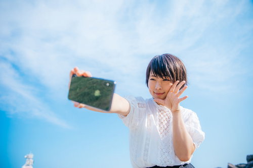 青空の下でスマートフォンで自撮りする女性