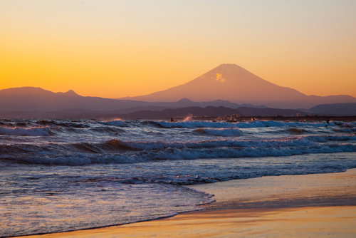 夕焼けに染まる富士山と押し寄せる波のビーチ風景