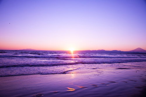 山並みを背景に静かに日が昇る海の波打ち際