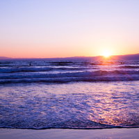 波寄せる浜辺の日の出と海でサーフィンを楽しむ朝焼けの風景の写真
