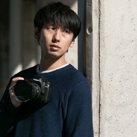 柱の陰からシャッターチャンスを狙う男性カメラマンの写真