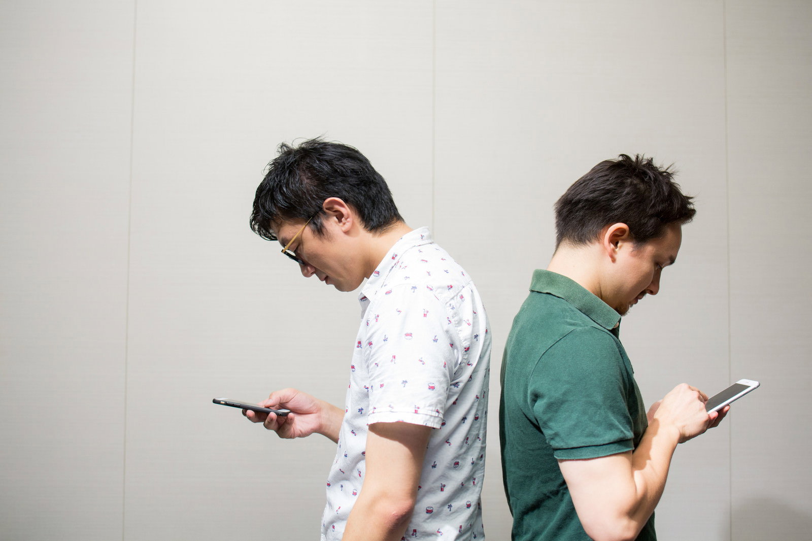 背中合わせでスマートフォンを見る2人の男性［モデル：Max_Ezaki ozpa］