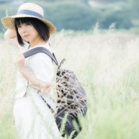 麦わら帽をかぶった彼女が草原でリュックを背負って振り返るの写真