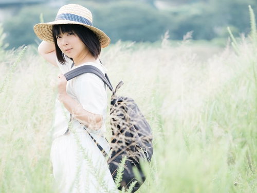 麦わら帽をかぶった彼女が草原でリュックを背負って振り返る