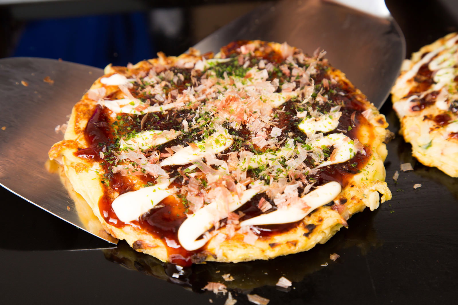 鉄板の上のお好み焼きにマヨネーズと鰹節、青のりをかけた
