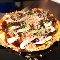 熱々の鉄板焼きお好み焼き、屋台の定番グルメの写真