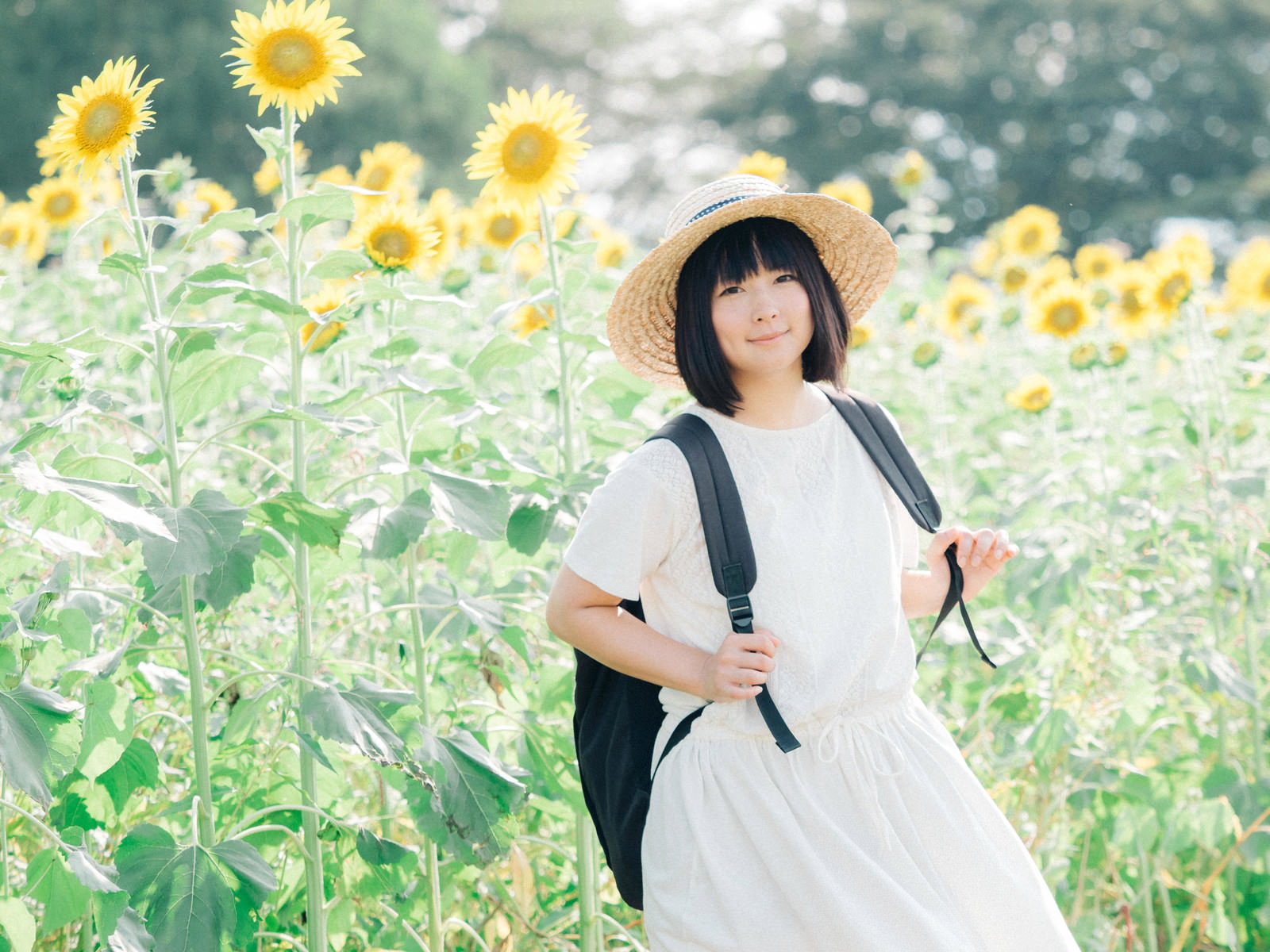 ひまわり畑で麦わら帽をかぶり笑顔を見せる女性［モデル：にゃるる］
