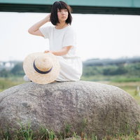石の上で遠くを見つめる麦わら女子の夏の休日の写真