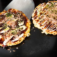 鉄板の上で焼かれたお好み焼き、ソースとマヨネーズがけの写真