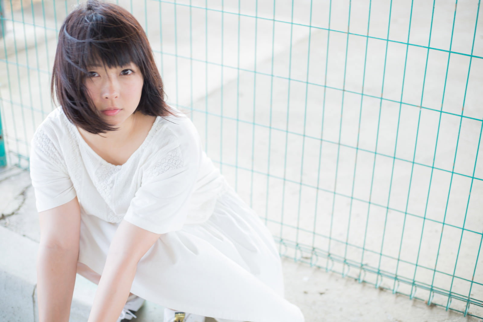 屋上でフェンス越しに外を見つめる白いワンピースの女性［モデル：にゃるる］