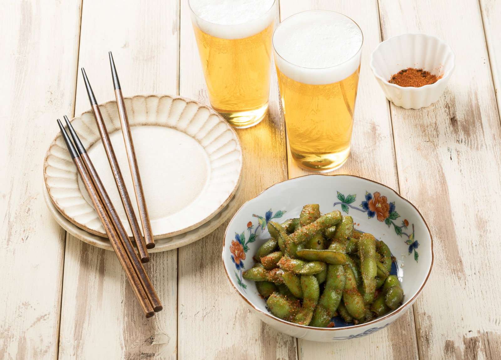 白い木製テーブルに置かれたビールグラスと七味唐辛子で味付けした枝豆