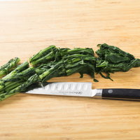 黒いまな板でほうれん草をざく切りする調理風景の写真