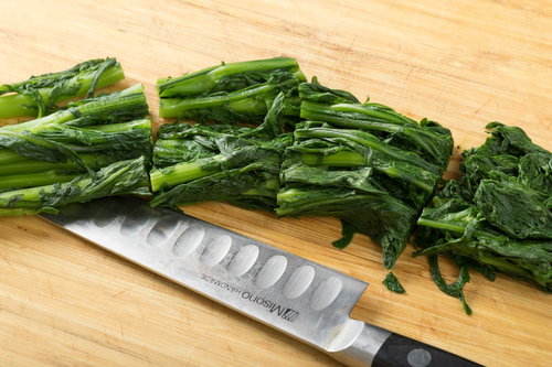 茹でて水気を絞ったほうれん草を木製まな板でざく切り