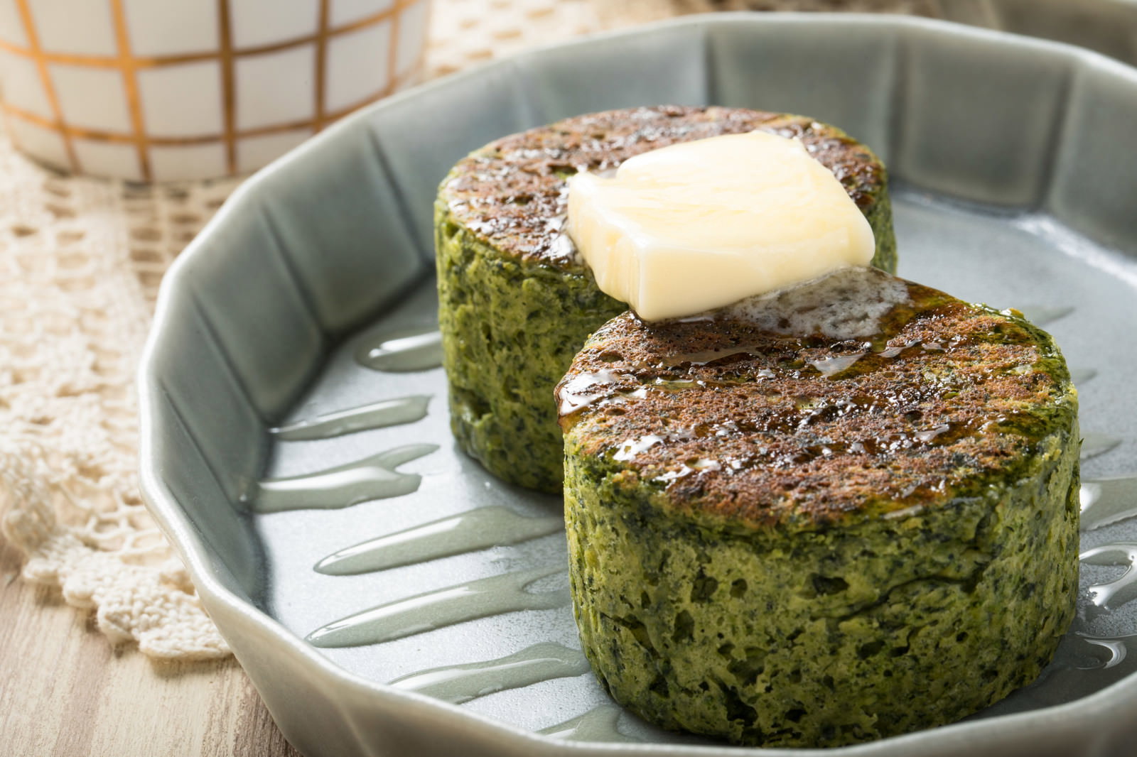 白い皿に盛り付けられた緑色のほうれん草パンケーキとバター