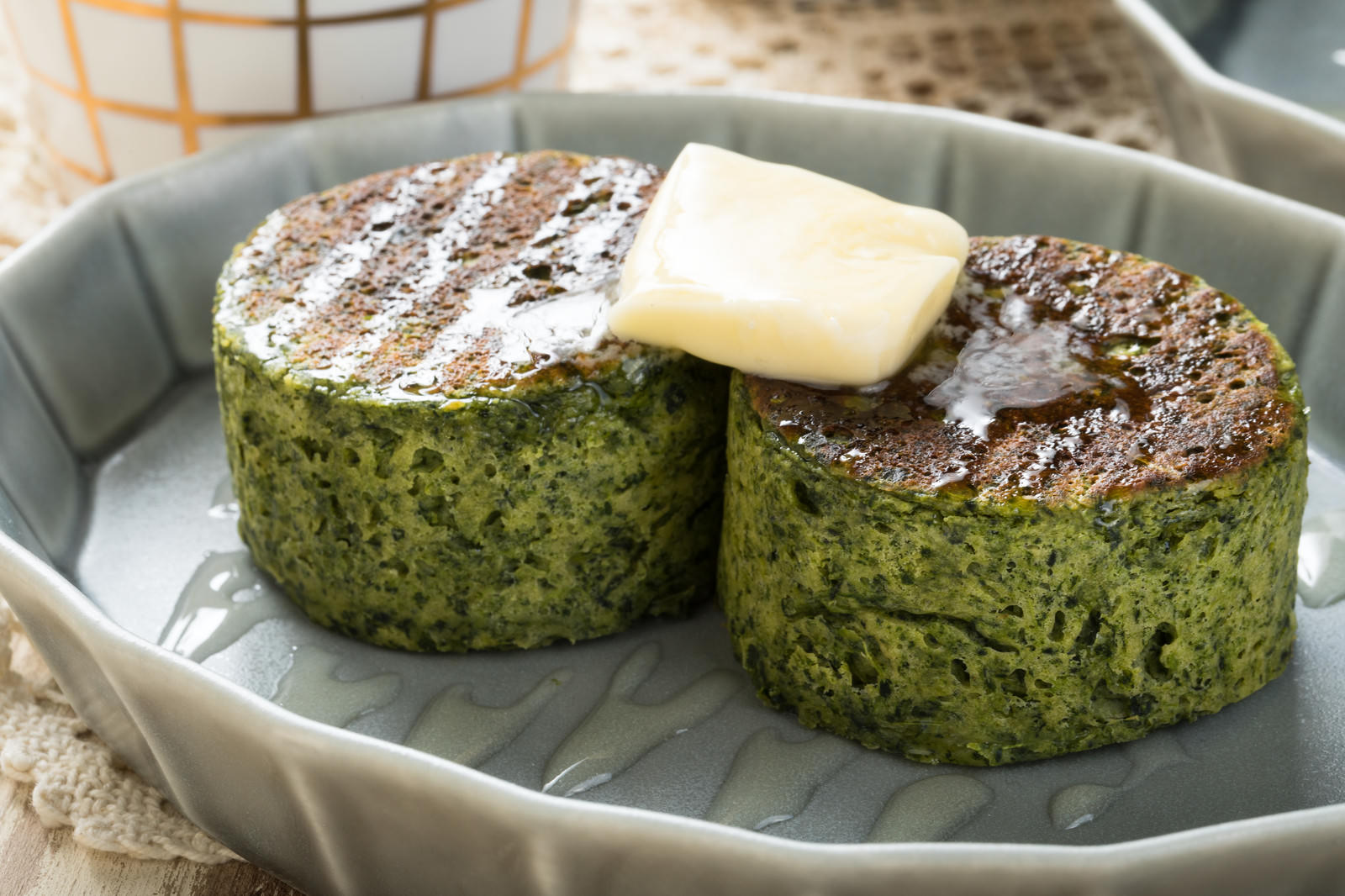 白いプレートに盛り付けられた緑色のほうれん草パンケーキとバター