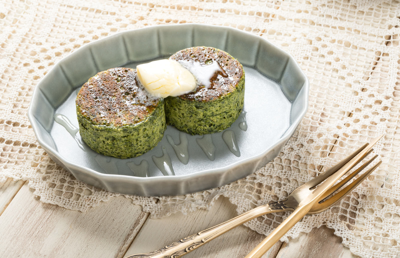 グレーの皿に盛り付けられたほうれん草入りの緑色パンケーキ2枚とクリーム