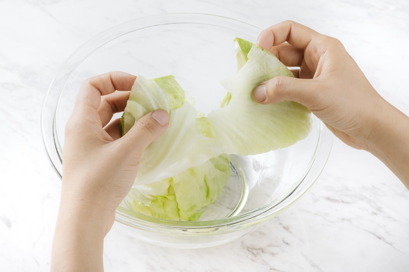 透明なボウルの上でレタスを手で千切っている様子