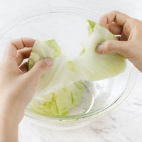 透明なボウルの上でレタスを手で千切る調理準備の写真