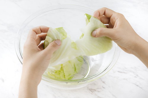 透明なボウルの上でレタスを手で千切る調理準備