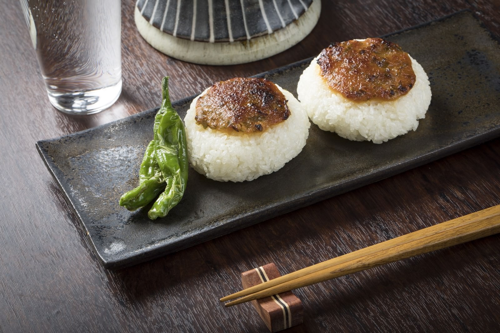 黒い長皿に盛った味噌焼きおにぎり2個と焼きししとう、箸を添えた夜食