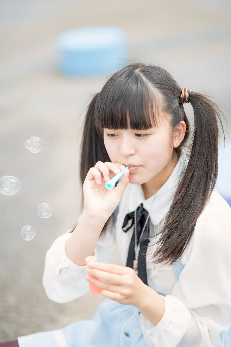 シャボン玉を吹くツインテール姿の女の子が制服を着ている［モデル：こころ］
