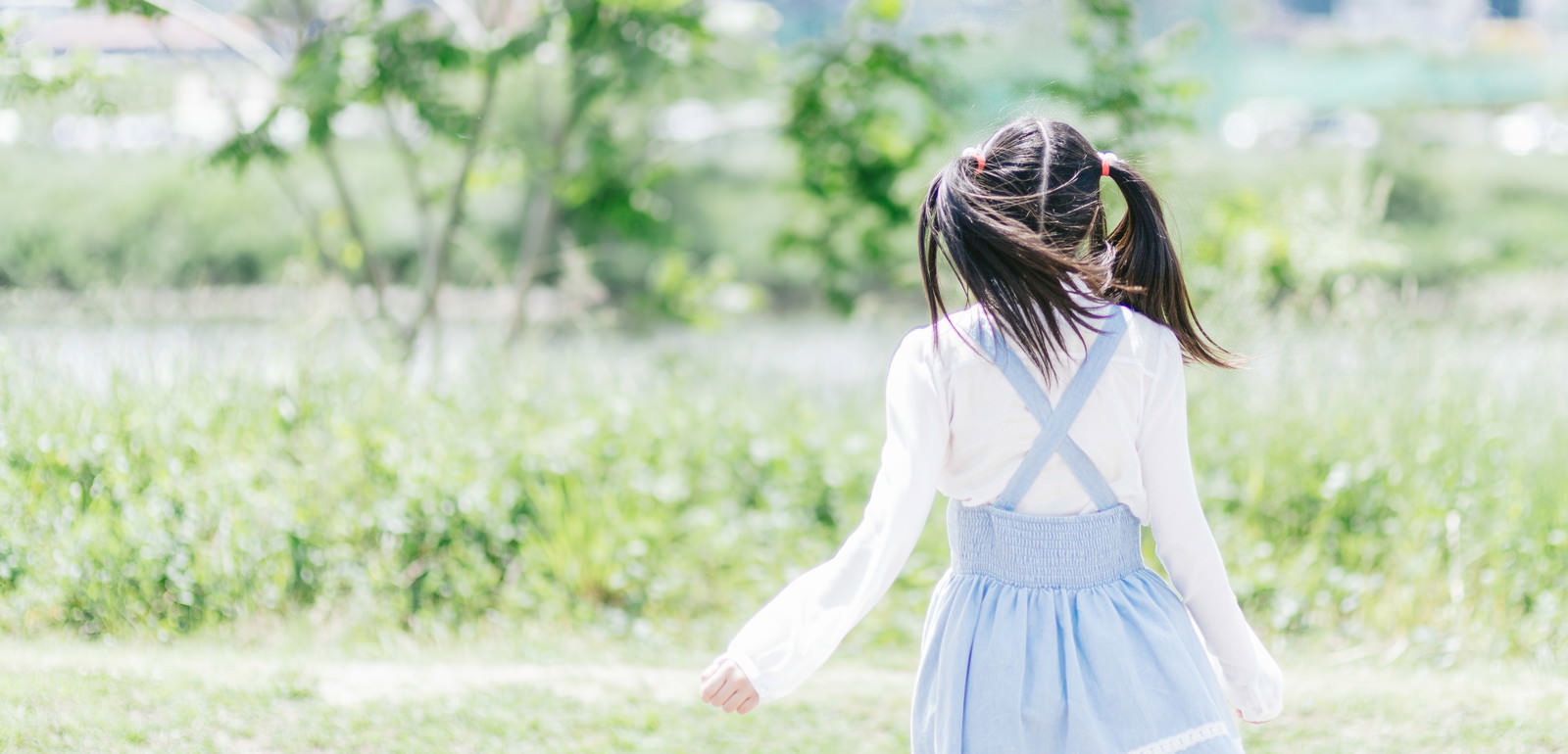 緑の公園に立つツインテール女の子の後ろ姿［モデル：こころ］