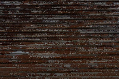 茶色いペンキが剥がれて劣化した横張りの木製板壁