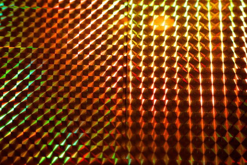緑と橙色に光るホログラムの立体格子パターンとプリズム