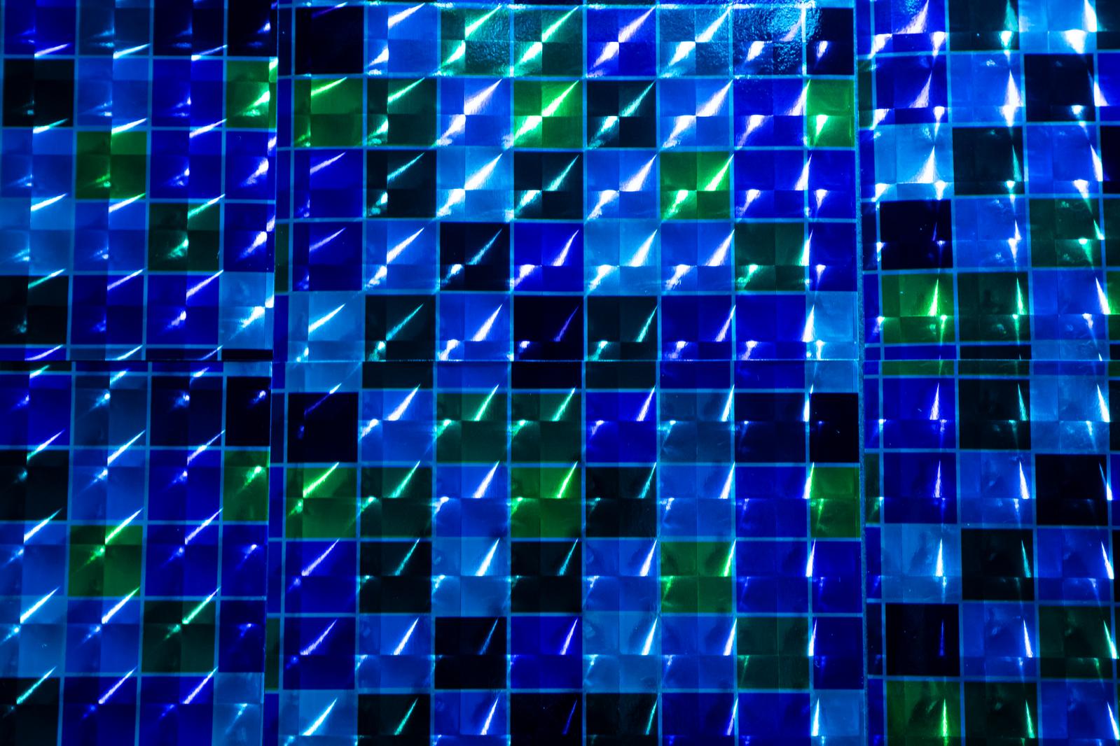 青と緑の正方形が格子状に並び光を反射するホログラムシートの接写