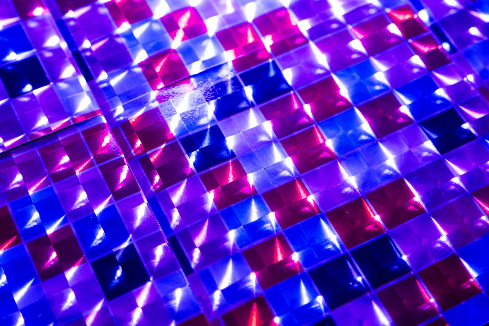 Diagonal close-up image of a grid-patterned hologram sheet glowing in blue, purple, and pink