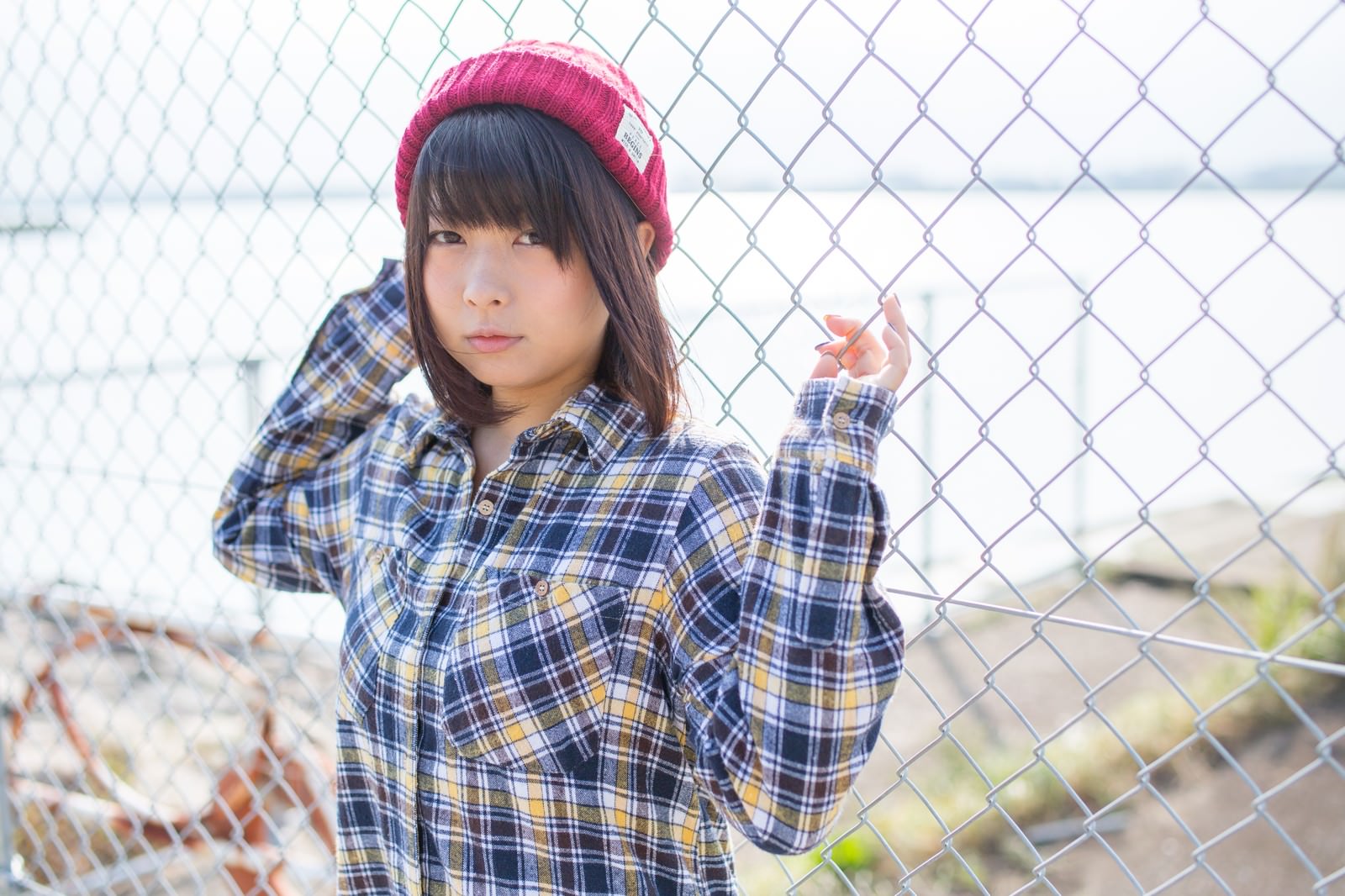 金網フェンスにもたれるニット帽の女性［モデル：にゃるる］