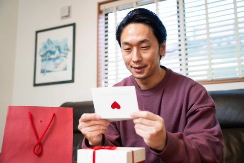 ラブレターを読んでにんまりする紫色セーターの男性