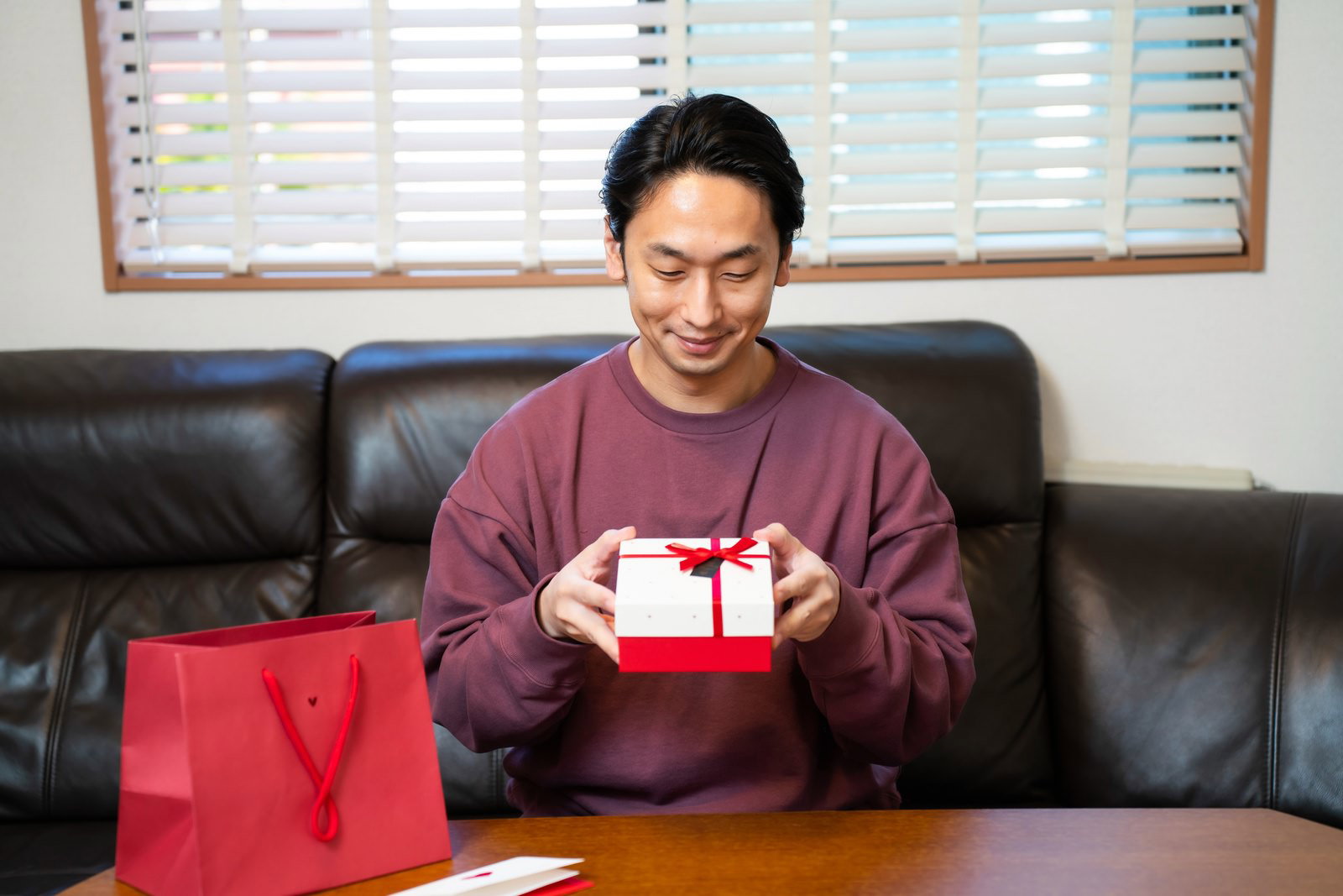 バレンタインの赤いプレゼント箱を持って笑顔を見せる男性［モデル：大川竜弥］